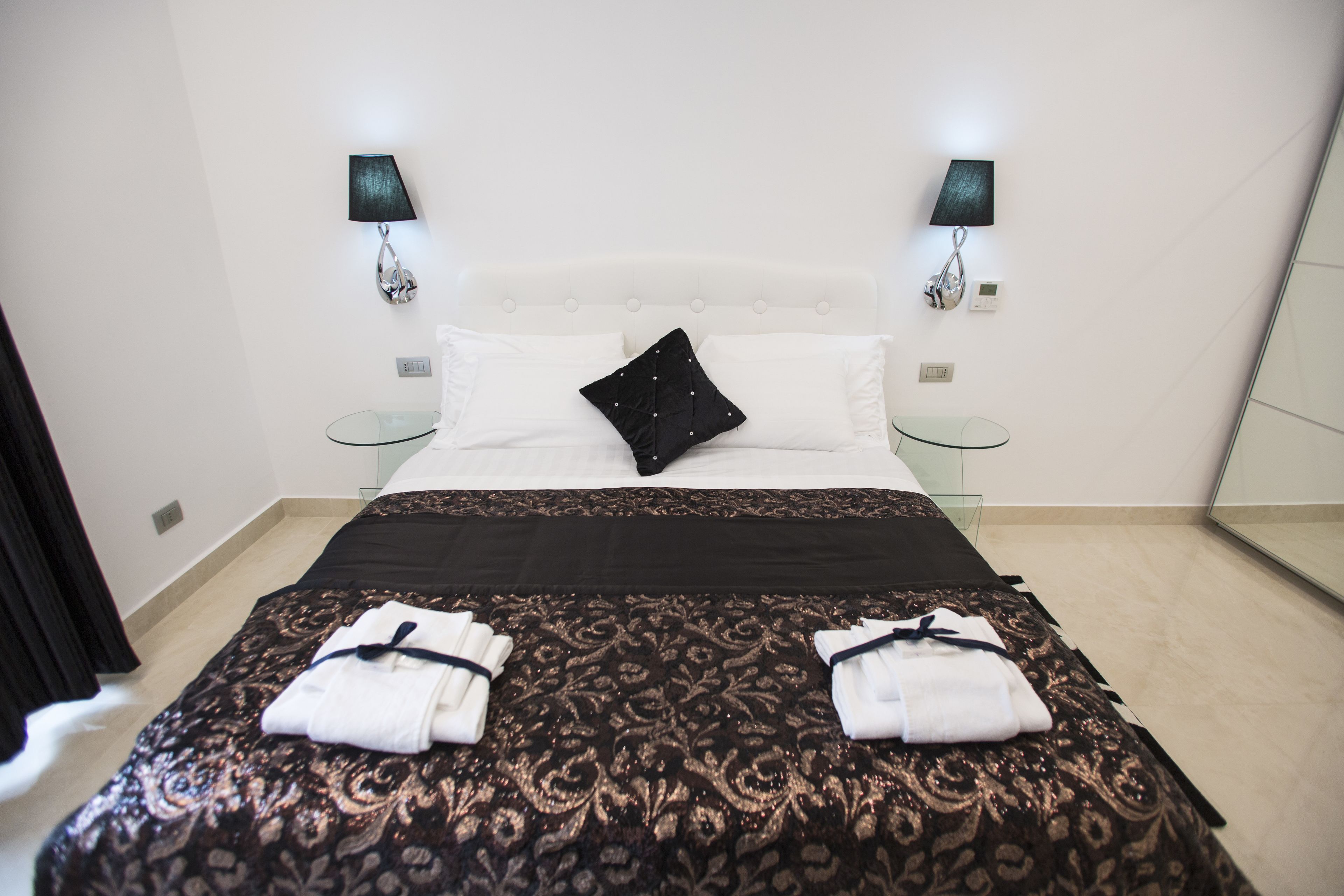Una habitación de hotel con una cama, dos lámparas de noche, una mesita de vidrio y un espejo.
