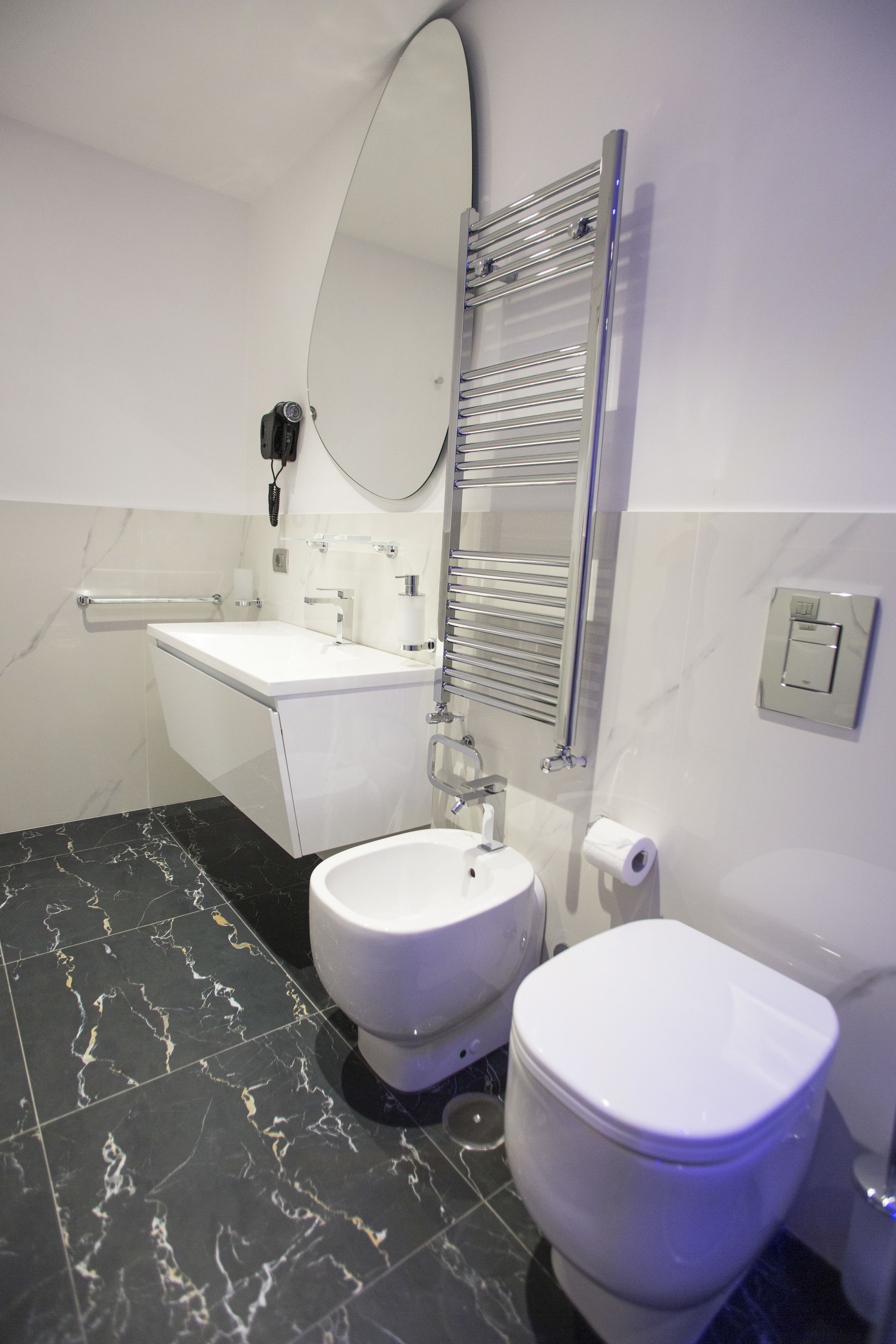 A modern bathroom with a white toilet, a bidet, a sink, and a mirror.