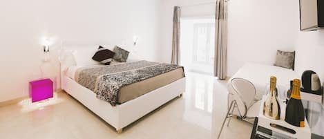 A modern hotel room with a bed, bedside table, and a small desk with a chair.