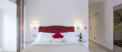A hotel room with a large bed, two bedside tables, a red headboard, and a glass partition wall.