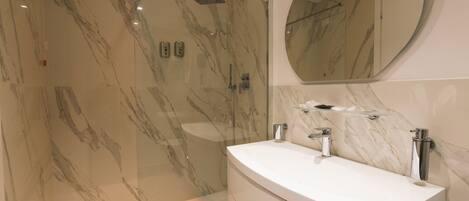 A modern bathroom with a marble shower, a round mirror, and a white vanity.