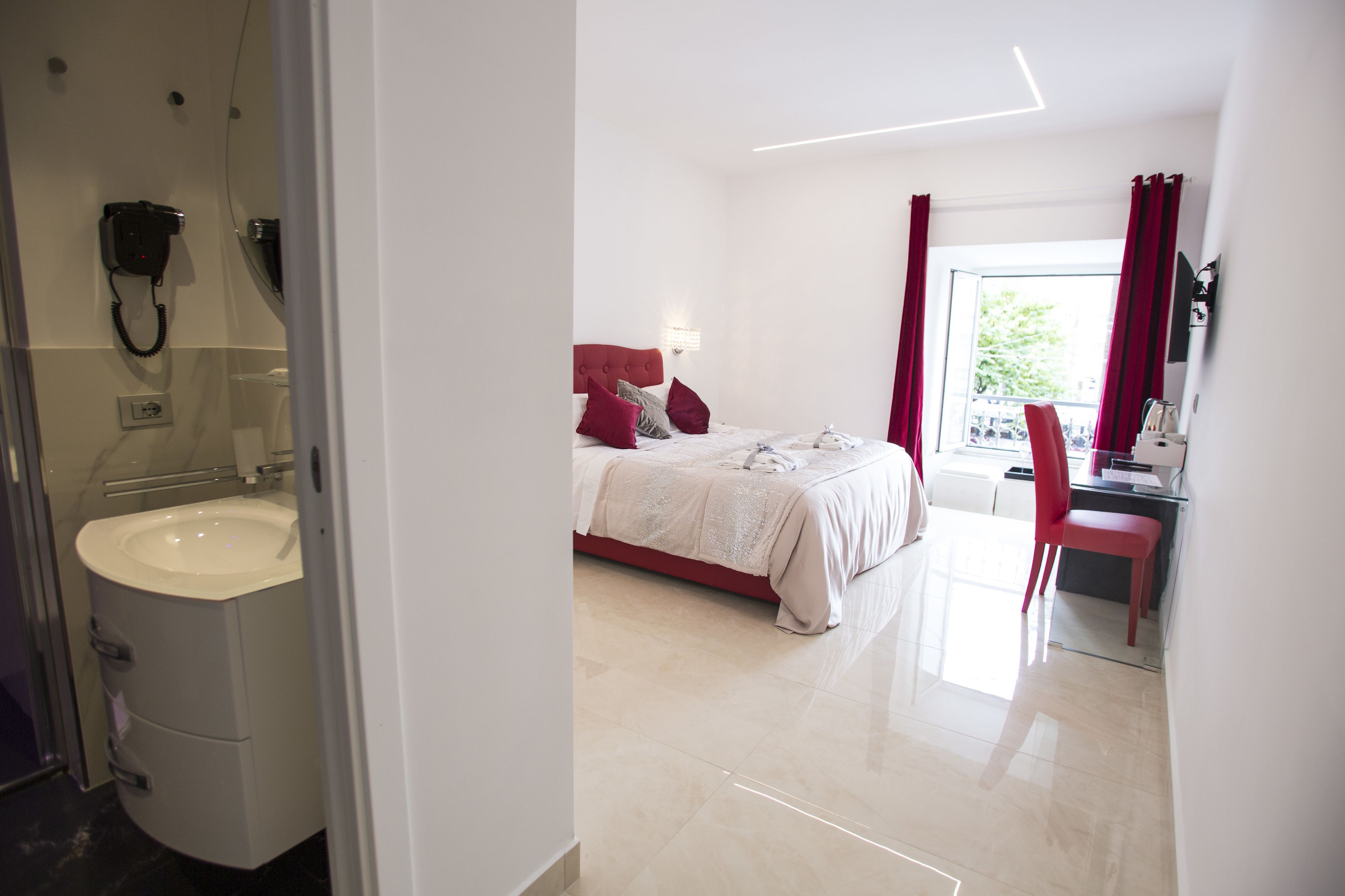 A hotel room with a bed, a desk, a chair, a bathroom with a sink, and a shower.