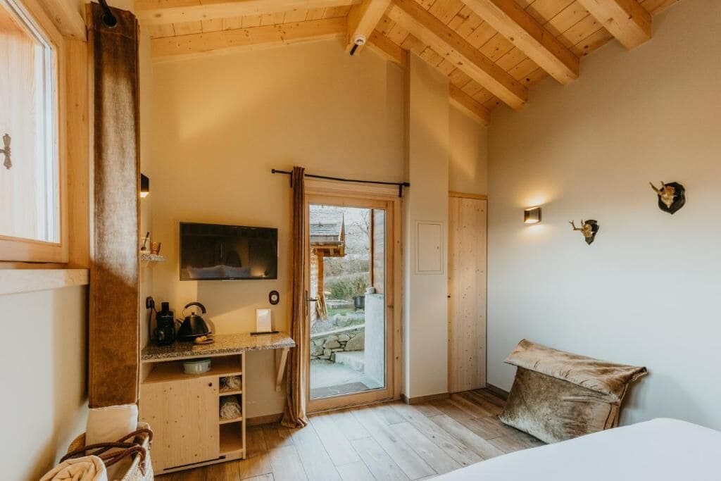 Una habitación con techo de madera, una cama, un escritorio pequeño con hervidor y televisor.