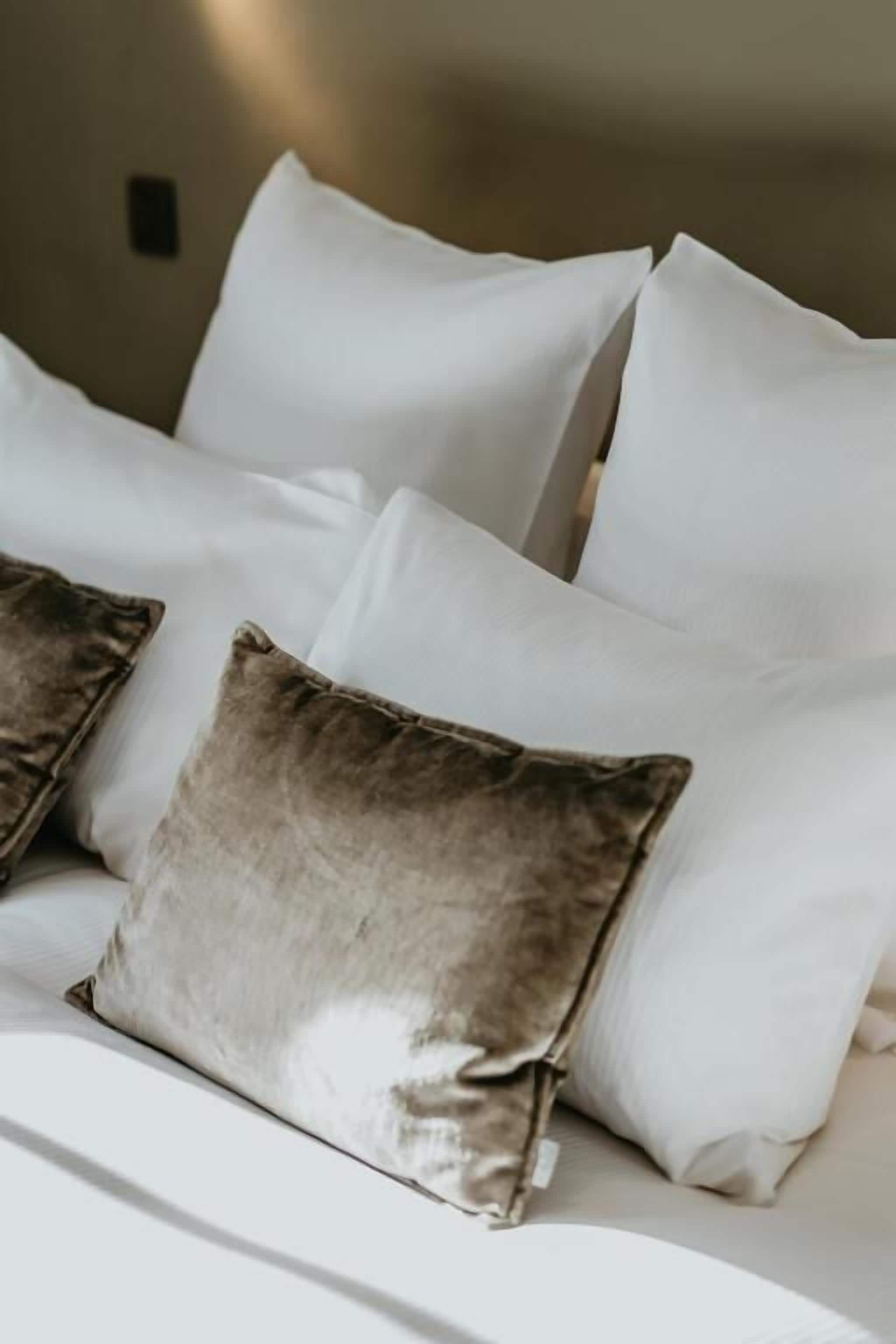 A bed with white bedding and two pillows, one of which is brown.