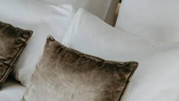 A bed with white bedding and two pillows, one of which is brown.