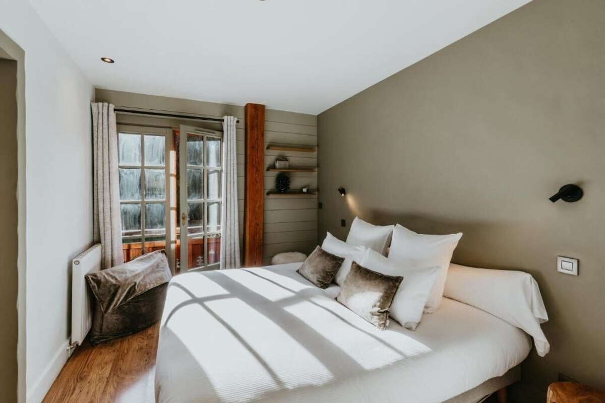 A bedroom with a bed, pillows, a window with curtains, and a radiator.