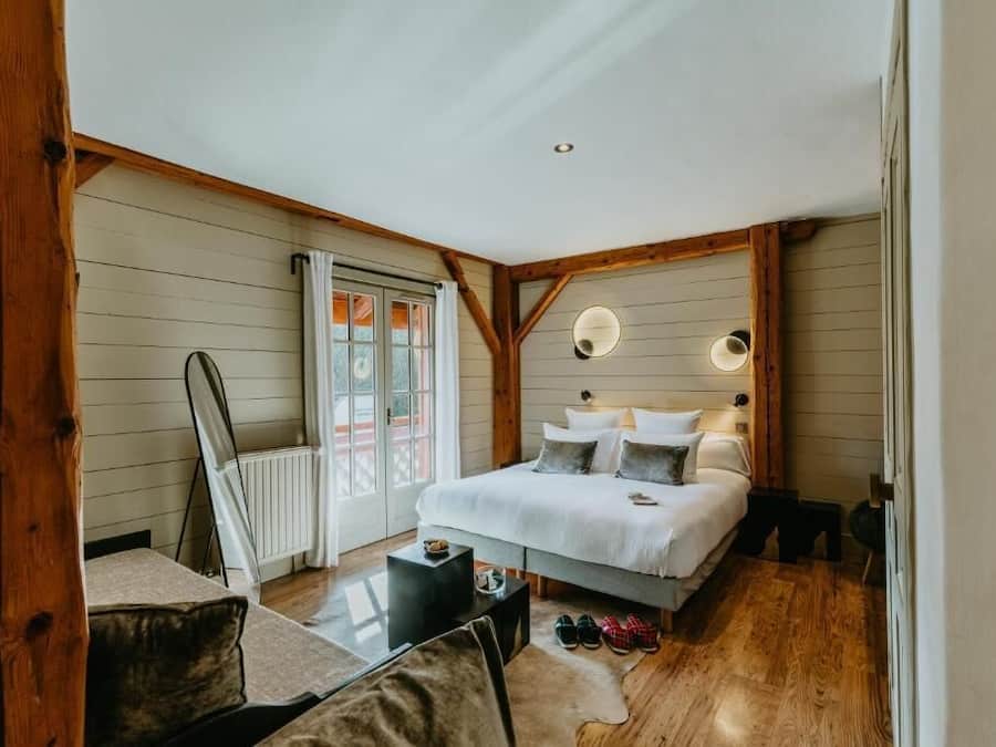A bedroom with a bed, a small table, a chair, a radiator, and a window with curtains.