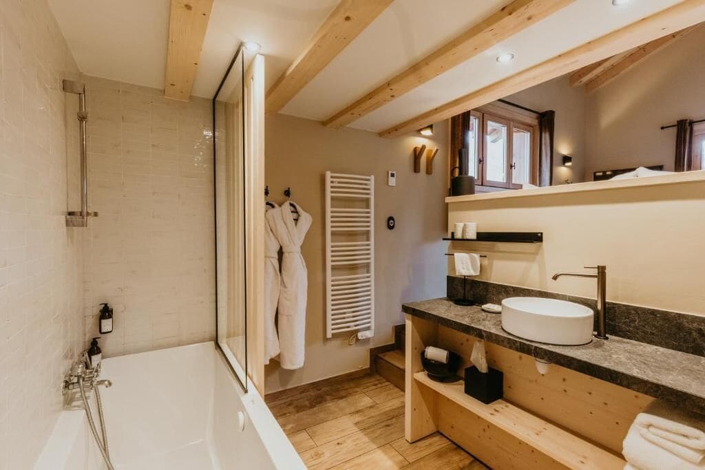 Une salle de bain moderne avec une baignoire, un grand miroir et des poutres en bois au plafond.