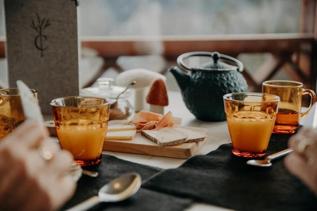 Una mesa con vasos de líquido ámbar, queso y una tetera, evocando un ambiente para comer.