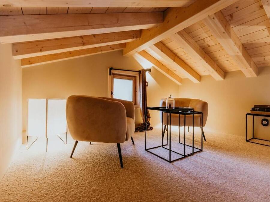 Una habitación con techo alto, vigas de madera, piso alfombrado, una mesa con sillas y una puerta que da al exterior.