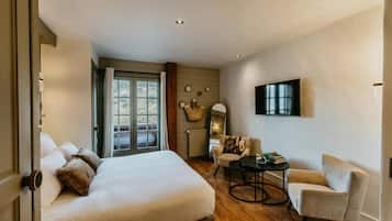 Una habitación de hotel con una cama grande, una mesa redonda, un sofá, un televisor y un ventanal con cortinas.