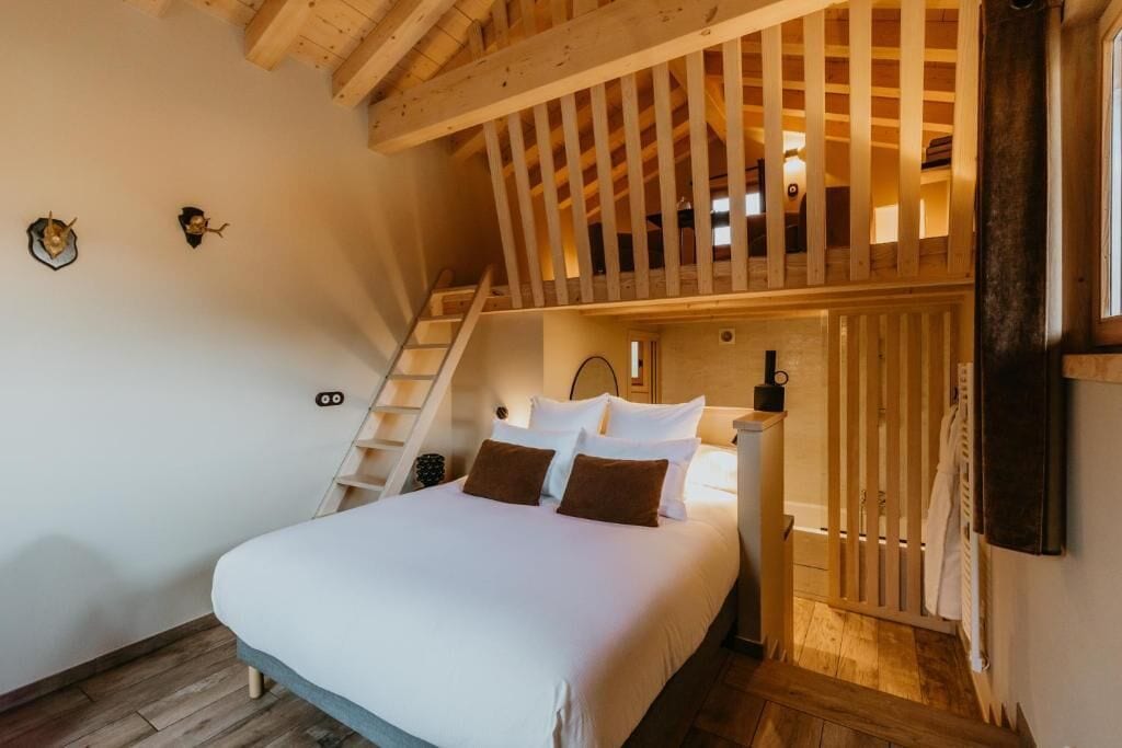 Een slaapkamer met een bed, nachtkastje, lamp, houten ladder en een raam.
