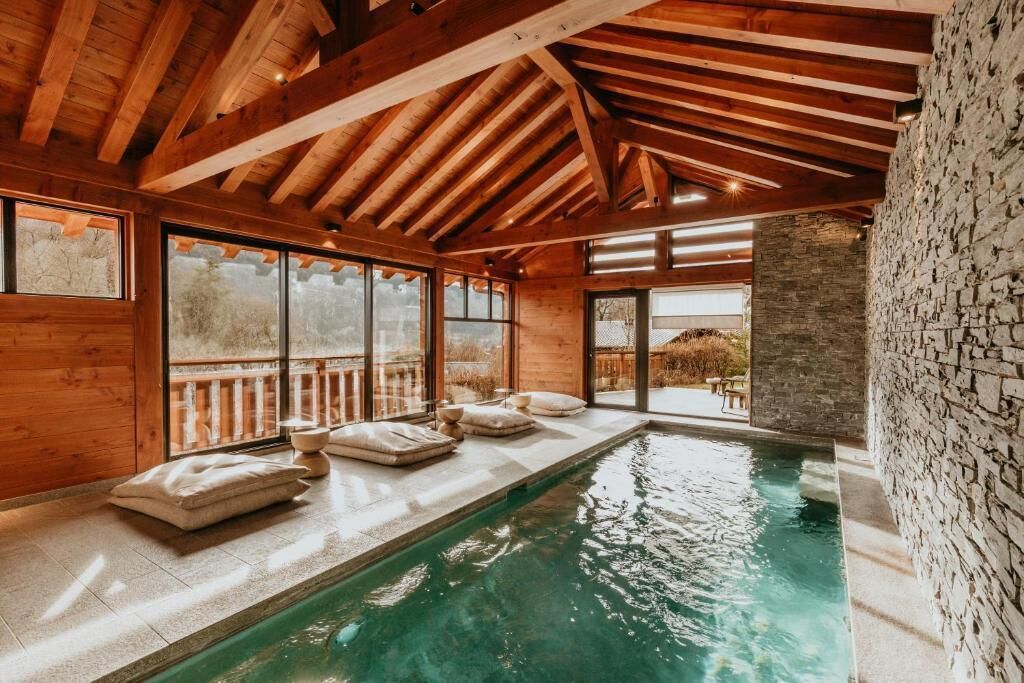 Interior de madera con piscina, paredes de piedra y ventanas grandes.