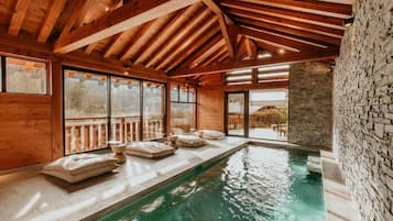 Interior de madera con piscina, paredes de piedra y ventanas grandes.