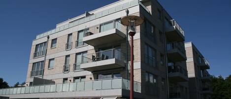 A modern multi-story building with balconies, large windows, and a flat roof.