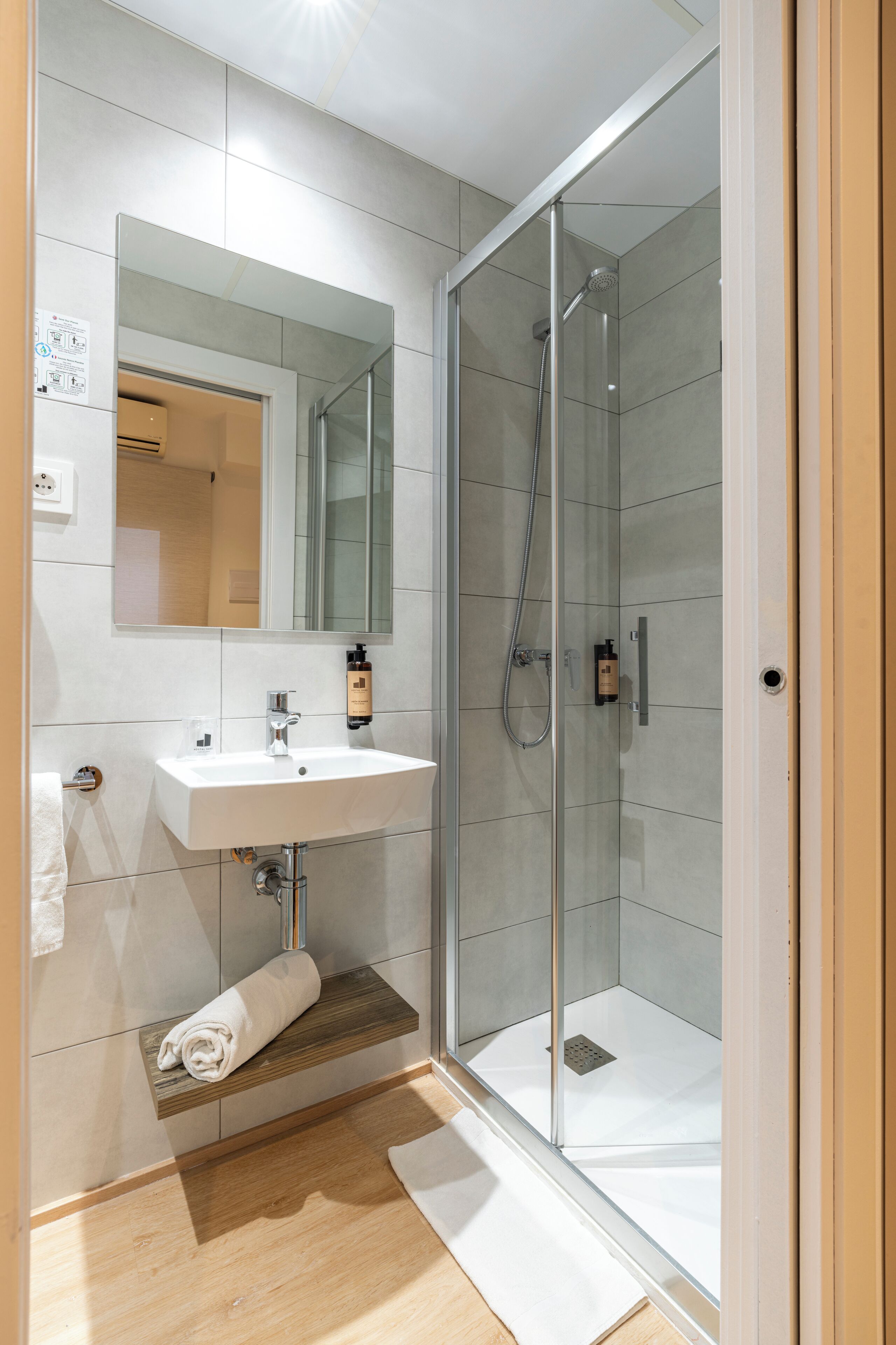 A modern bathroom with a glass-enclosed shower, a white sink, and a wooden shelf.