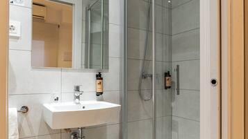A modern bathroom with a glass-enclosed shower, a white sink, and a wooden shelf.