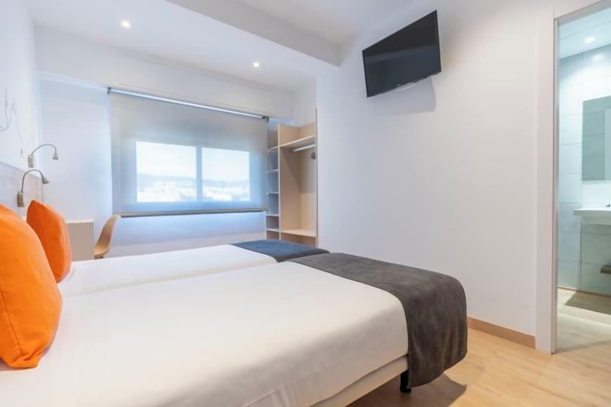 A modern bedroom with a large bed, a walk-in closet, a TV mounted on the wall, and a window with a view.