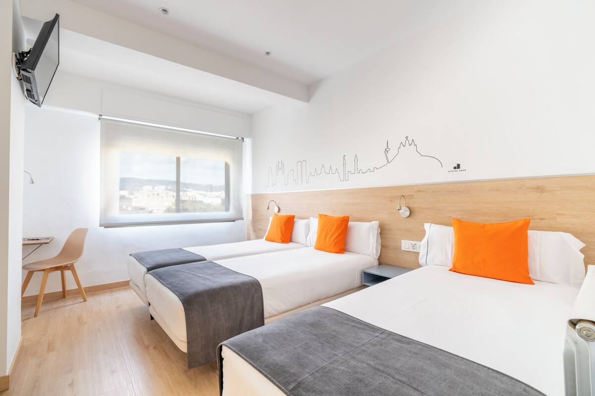 A hotel room with two beds, a desk, and a large window.