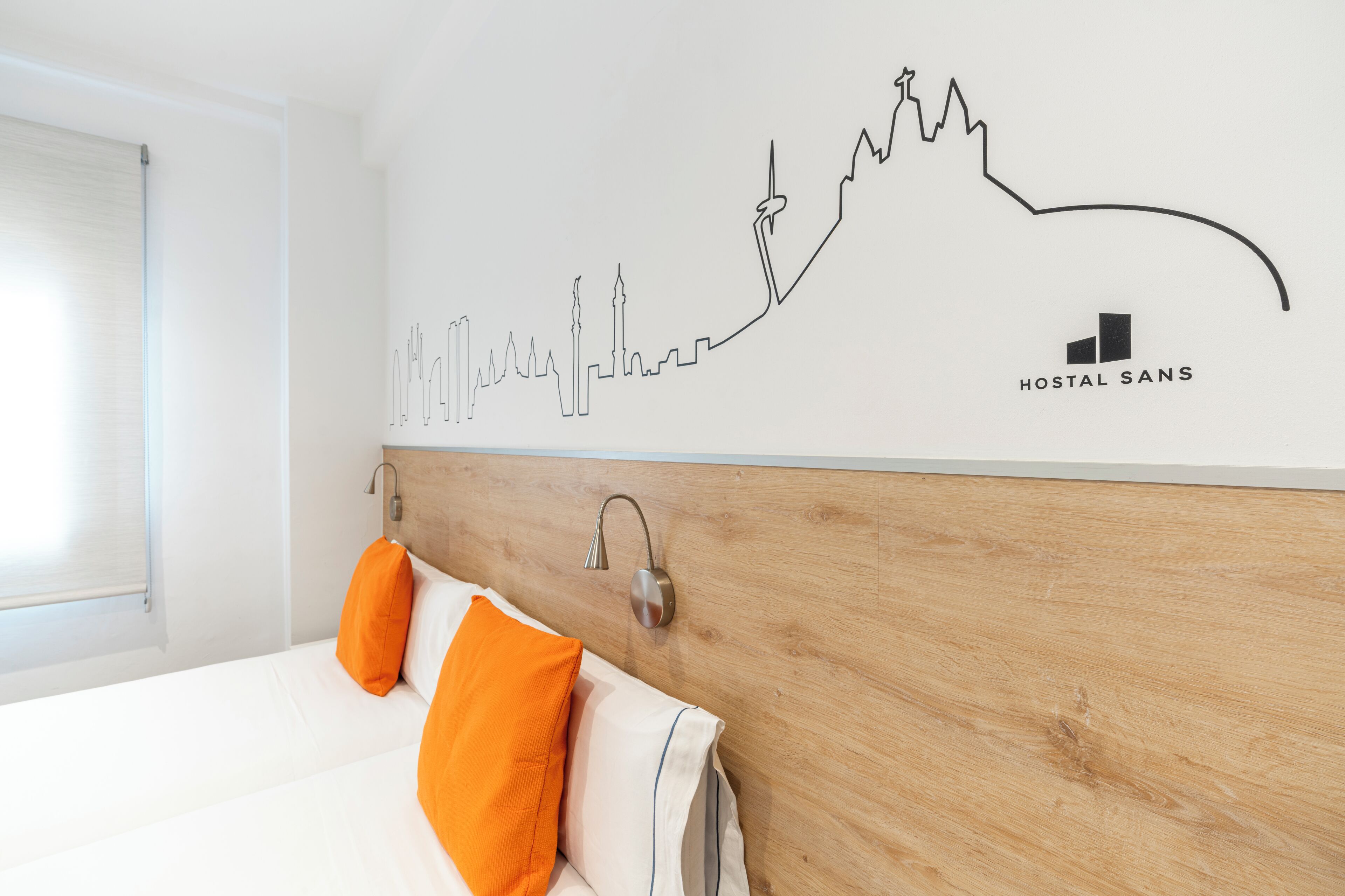 Habitación de hotel con cabecera de madera, ropa de cama blanca y almohadas anaranjadas. Un mural con el horizonte de la ciudad adorna la pared.