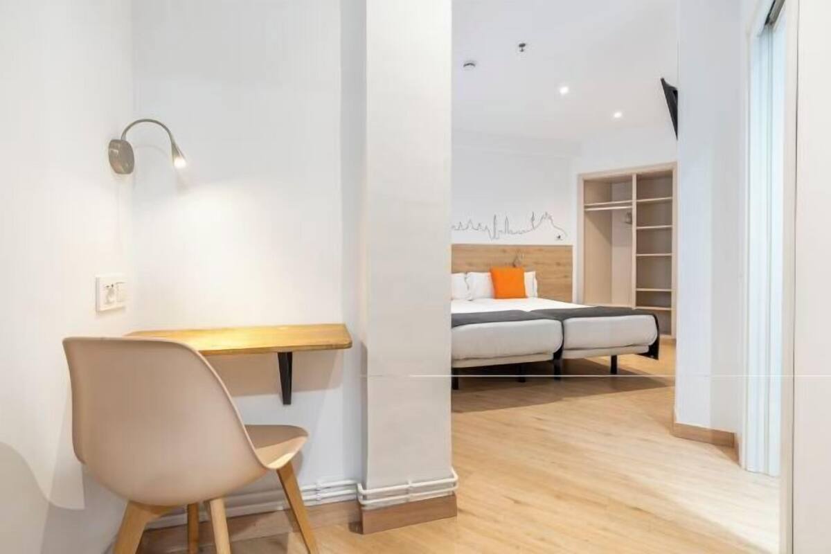 A modern room with a wooden desk, a chair, a bed with a headboard, and a wardrobe.