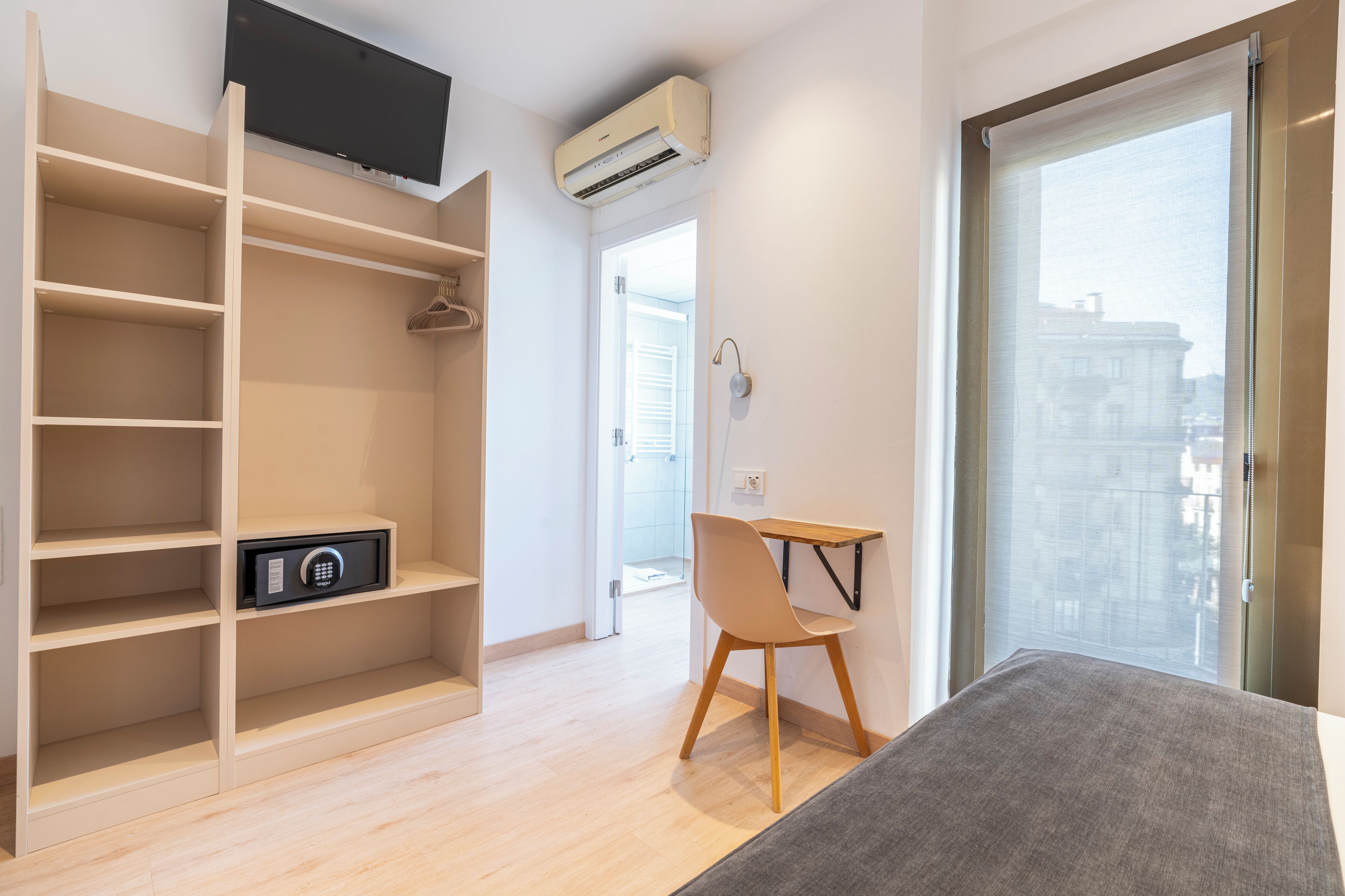 Una habitación moderna con televisión integrada, aire acondicionado, un escritorio con silla y un amplio ventanal con vista a la ciudad.
