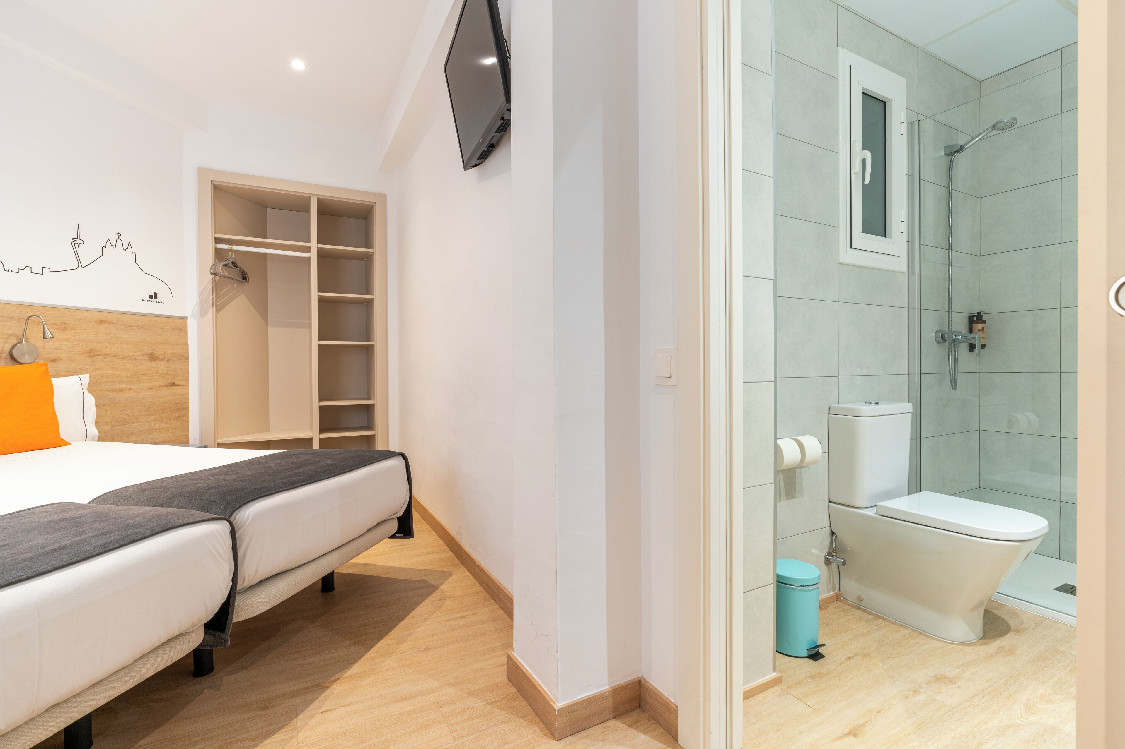A modern hotel room with a bed, a wardrobe, a TV, and a bathroom with a shower and toilet.