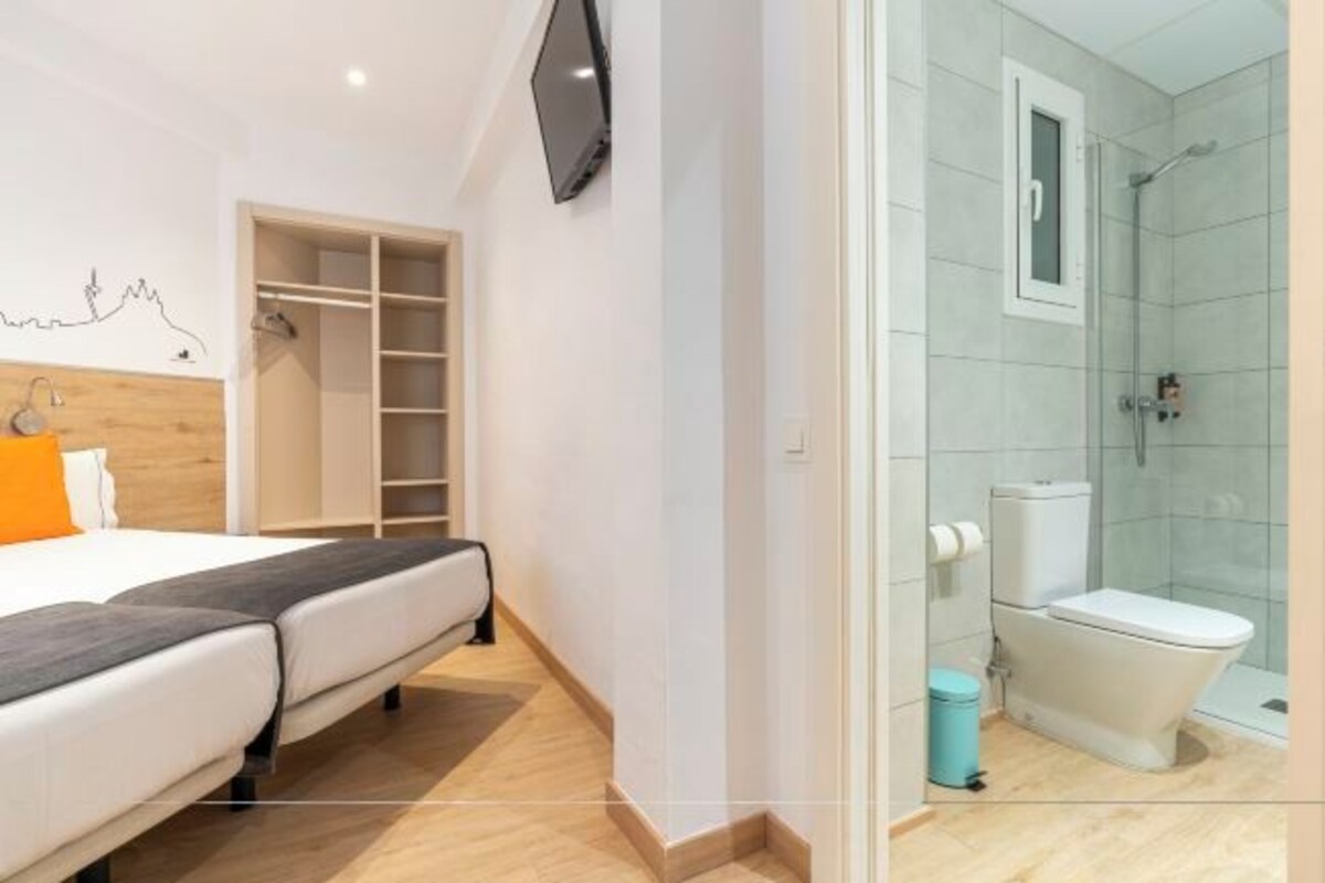A bedroom with a bed, a TV, a wardrobe, and a bathroom with a toilet and shower.