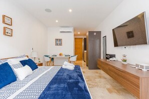 Habitación de hotel con cama, mesita de noche, televisor y escritorio con silla.