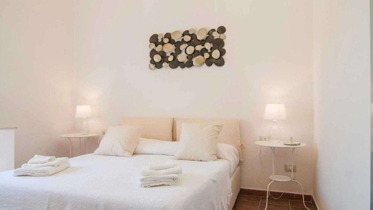 Una cama bien hecha con toallas dobladas, dos mesitas de noche con lámparas y una obra de arte en la pared sobre la cama.