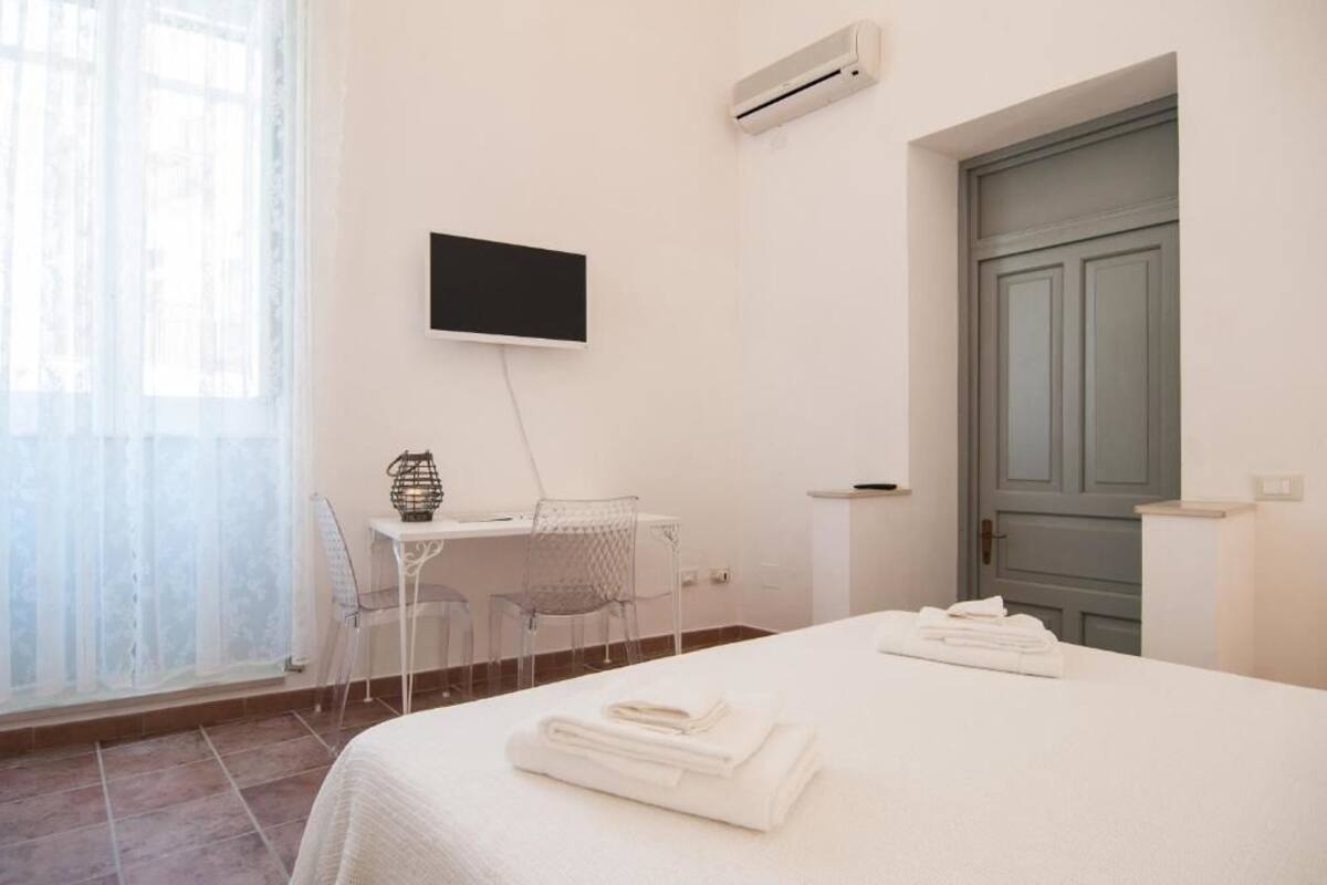 Habitación de hotel con cama, escritorio y silla, televisor montado en la pared y una puerta.