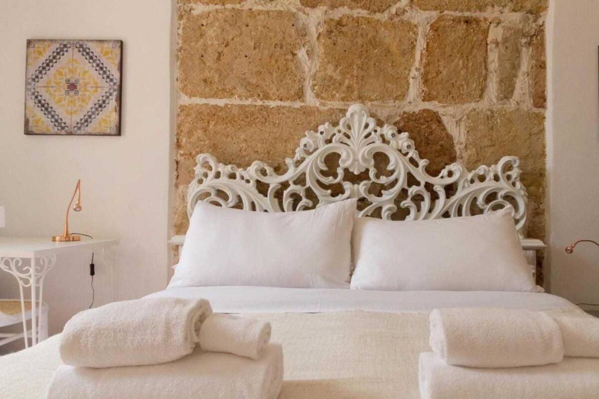 Una cama con una elaborada cabecera blanca, dos almohadas blancas y dos toallas enrolladas al frente.