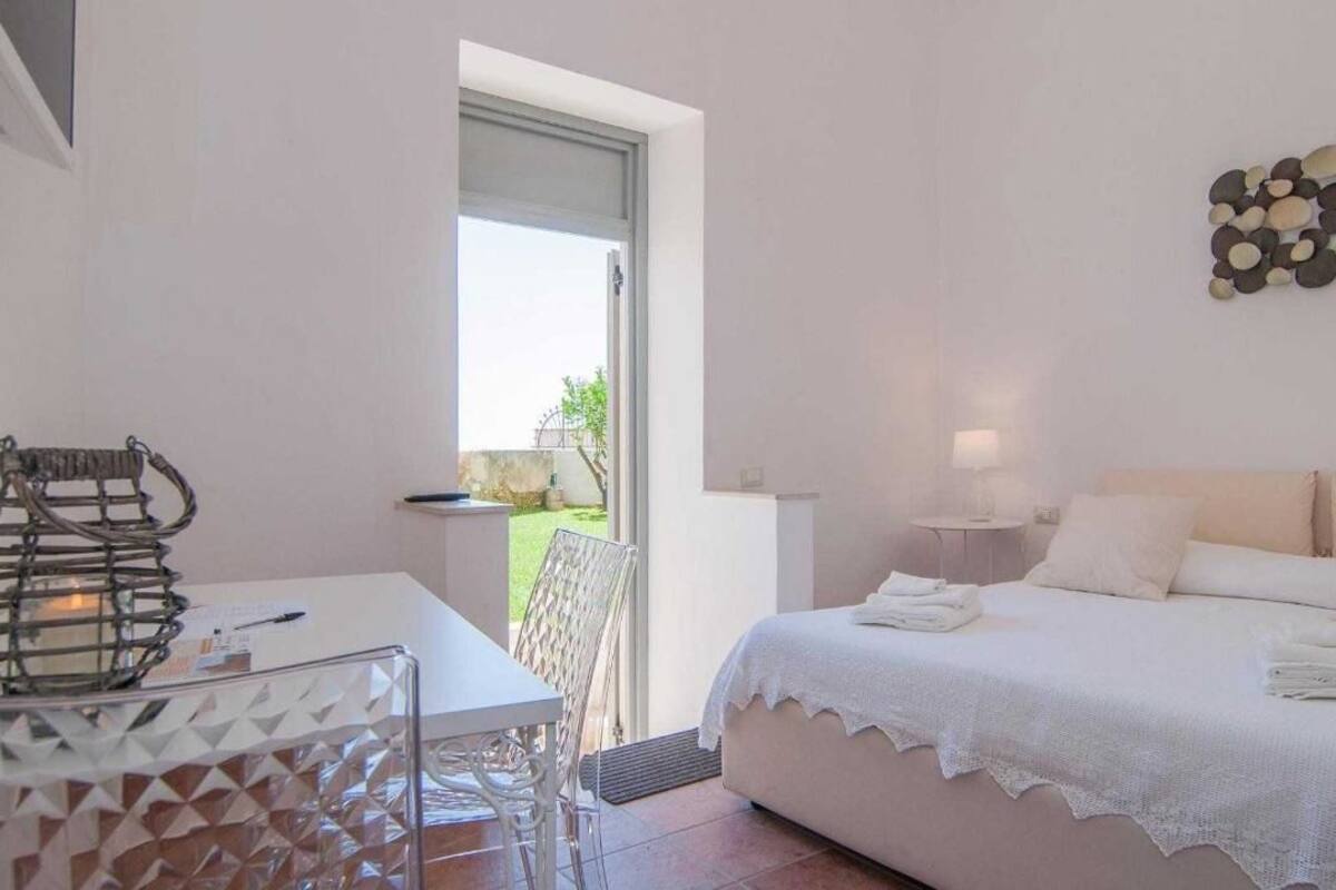 Un dormitorio con cama, escritorio y silla. Se ve follaje verde por la ventana.