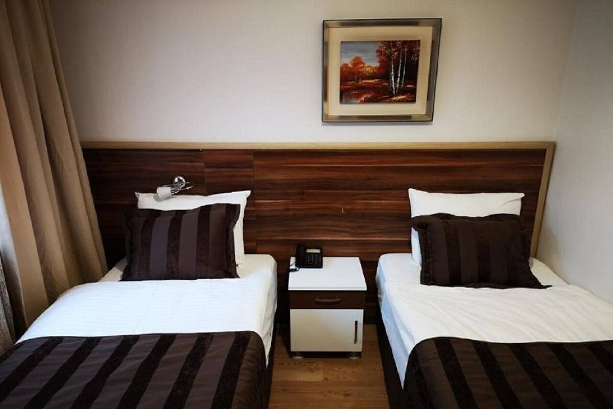 A hotel room with two beds, a nightstand with a phone, and a painting on the wall.