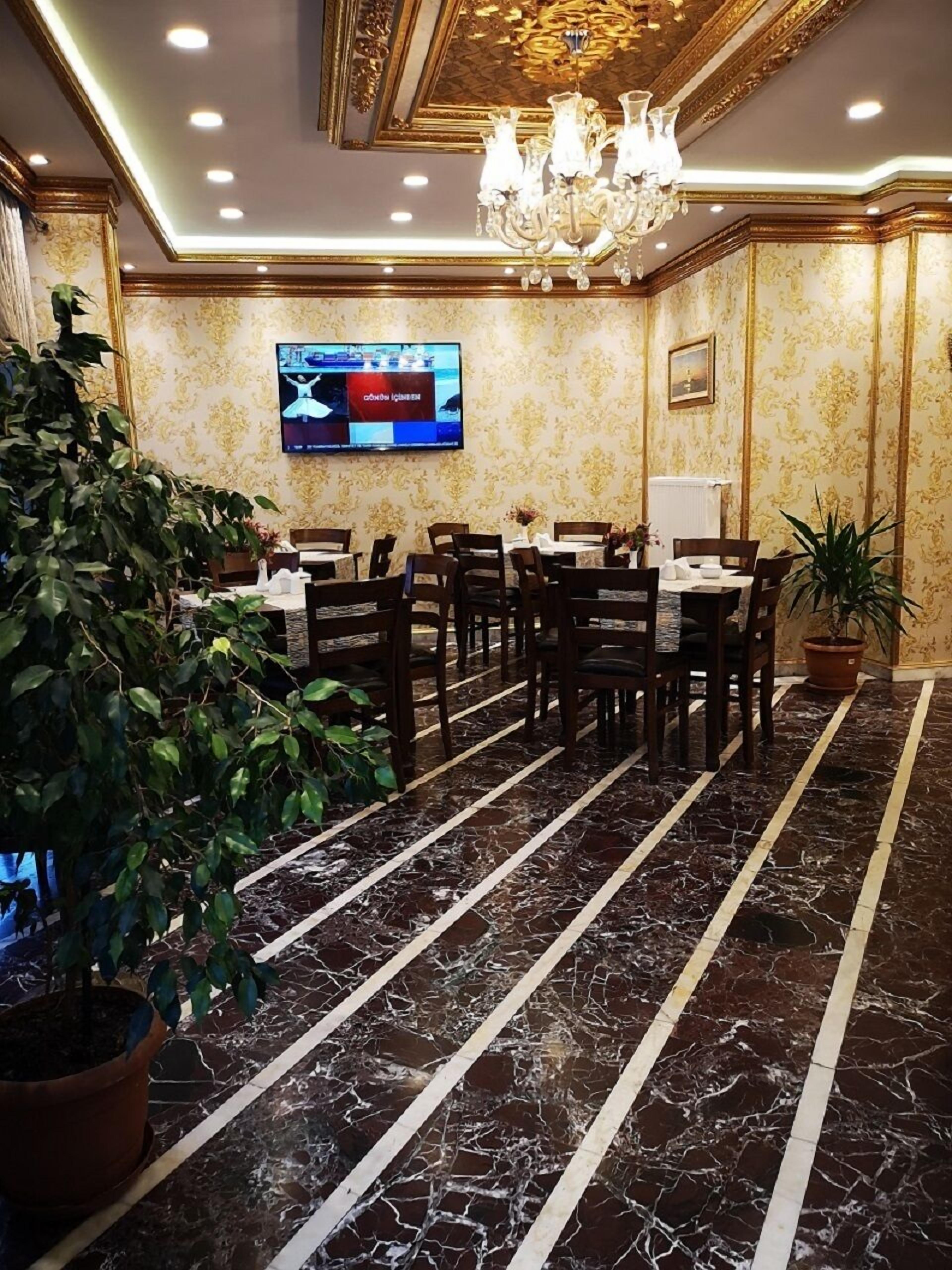 A dining area with a marble floor, tables, chairs, a chandelier, and a television screen.