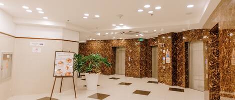 A spacious lobby with a marble floor, a potted plant, and an information board.