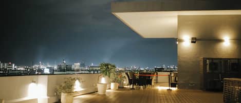 A rooftop terrace with a city view, potted plants, and a seating area.