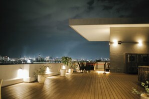 A rooftop terrace with a city view, potted plants, and a seating area.