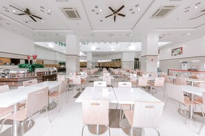 A spacious cafeteria with multiple tables and chairs, ceiling fans, and a modern design.
