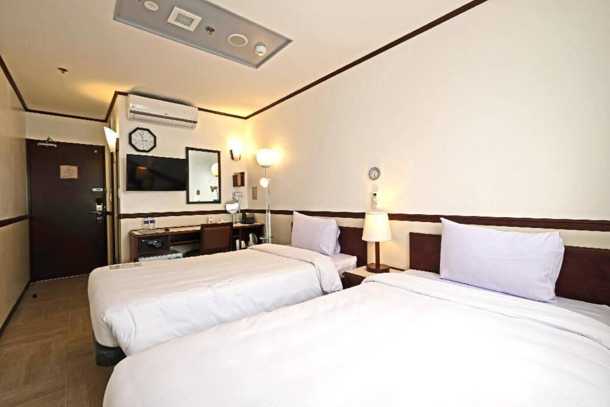 A hotel room with two beds, a desk with a chair, a mirror, and a clock on the wall.