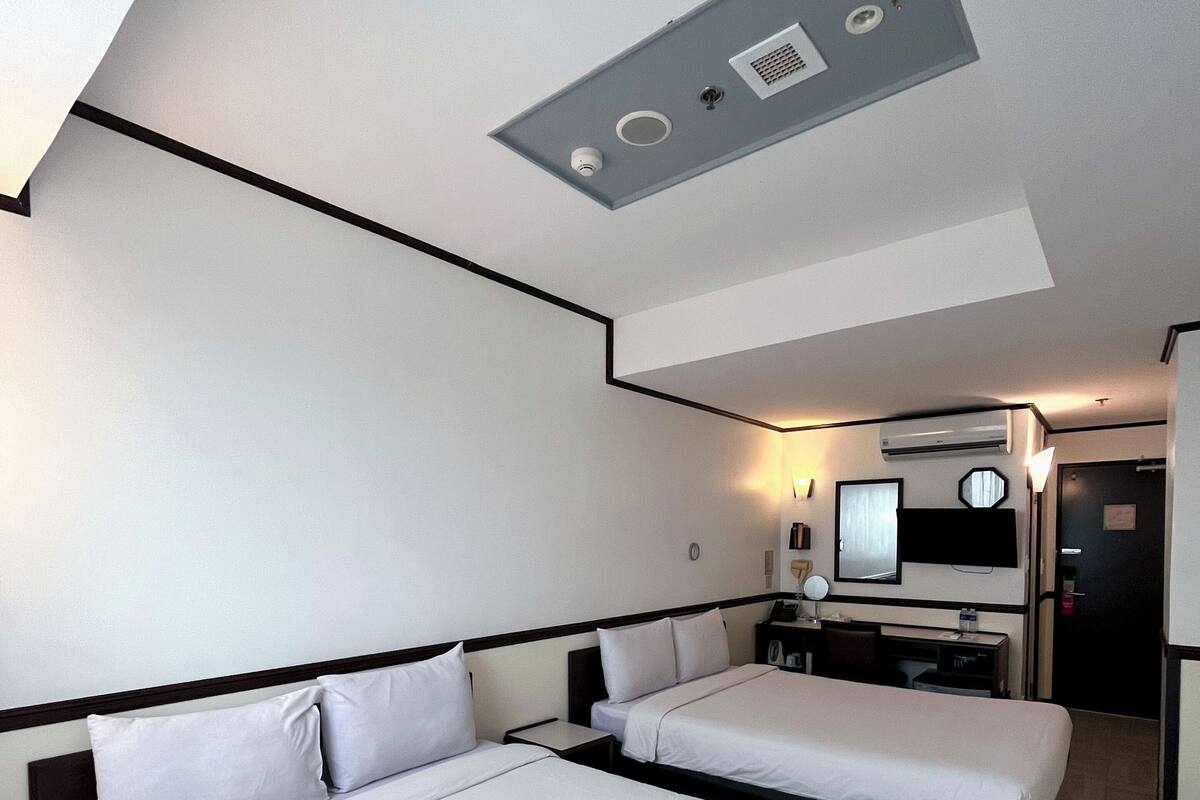 A hotel room with two beds, a desk, a chair, a television, and a ceiling light fixture.