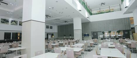 Un amplio comedor interior con varias mesas y sillas, ventiladores de techo e iluminación empotrada.