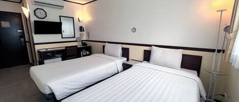 Habitación de hotel con dos camas, un escritorio, una silla, un espejo, un reloj y una lámpara.