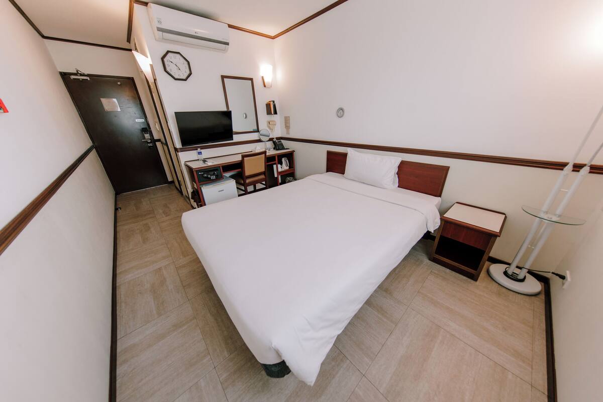 A hotel room with a bed, desk, chair, TV, and a bedside table.