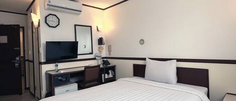 Habitación de hotel con cama, escritorio con ordenador, espejo, reloj y aire acondicionado.