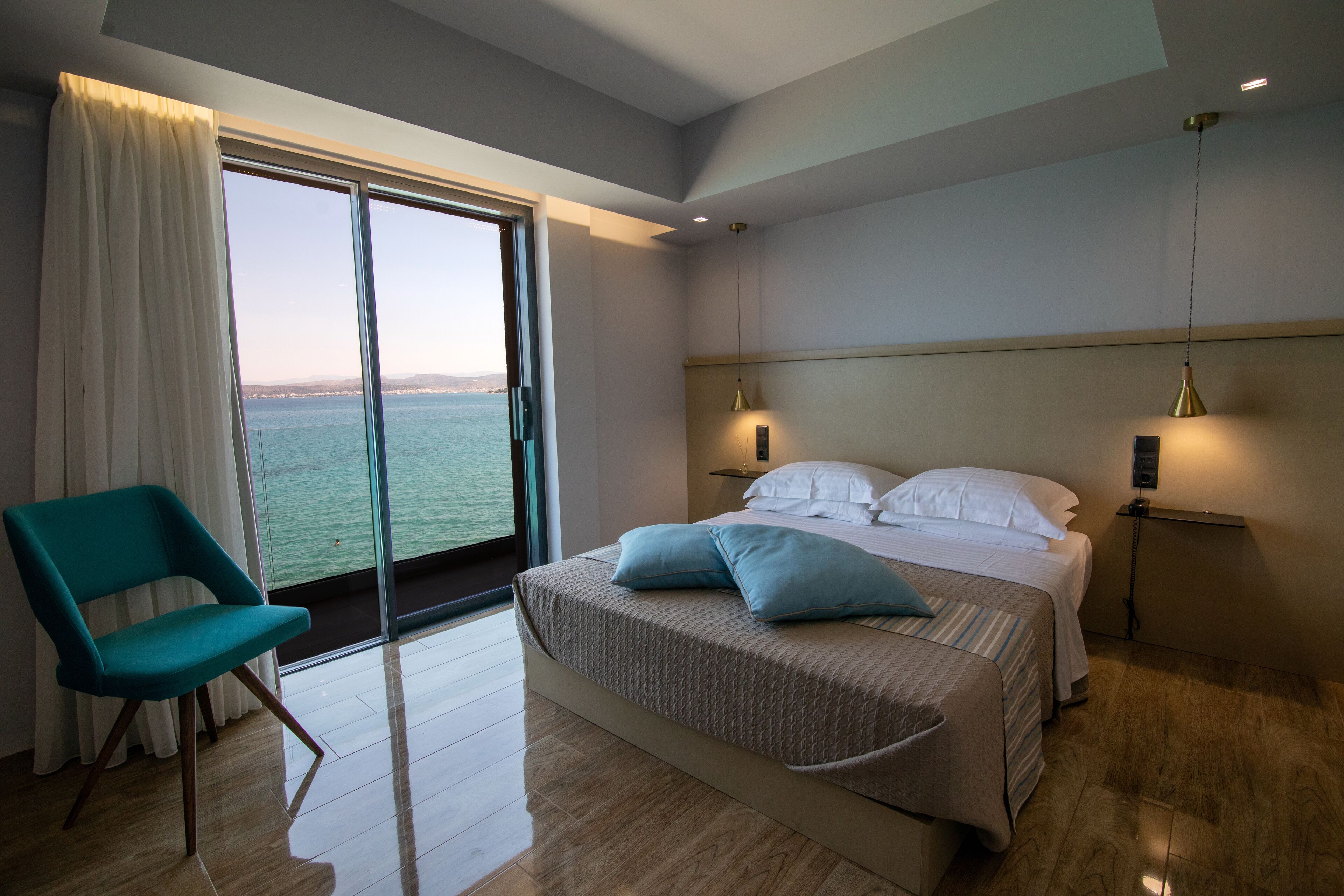 Un dormitorio moderno con una cama grande, una silla color turquesa y vista al mar a través de una puerta corrediza.