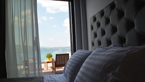 Une chambre avec un grand lit, une vue sur la mer par la fenêtre et une petite table avec une plante.