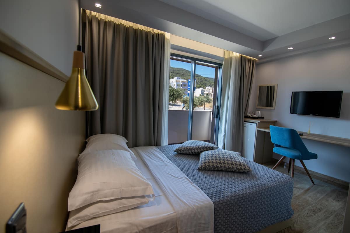 Habitación de hotel con cama, escritorio, silla, televisión y ventana con cortinas.
