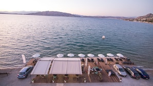 Une terrasse au bord de l’eau, avec des sièges d’extérieur, des parasols et des voitures garées.
