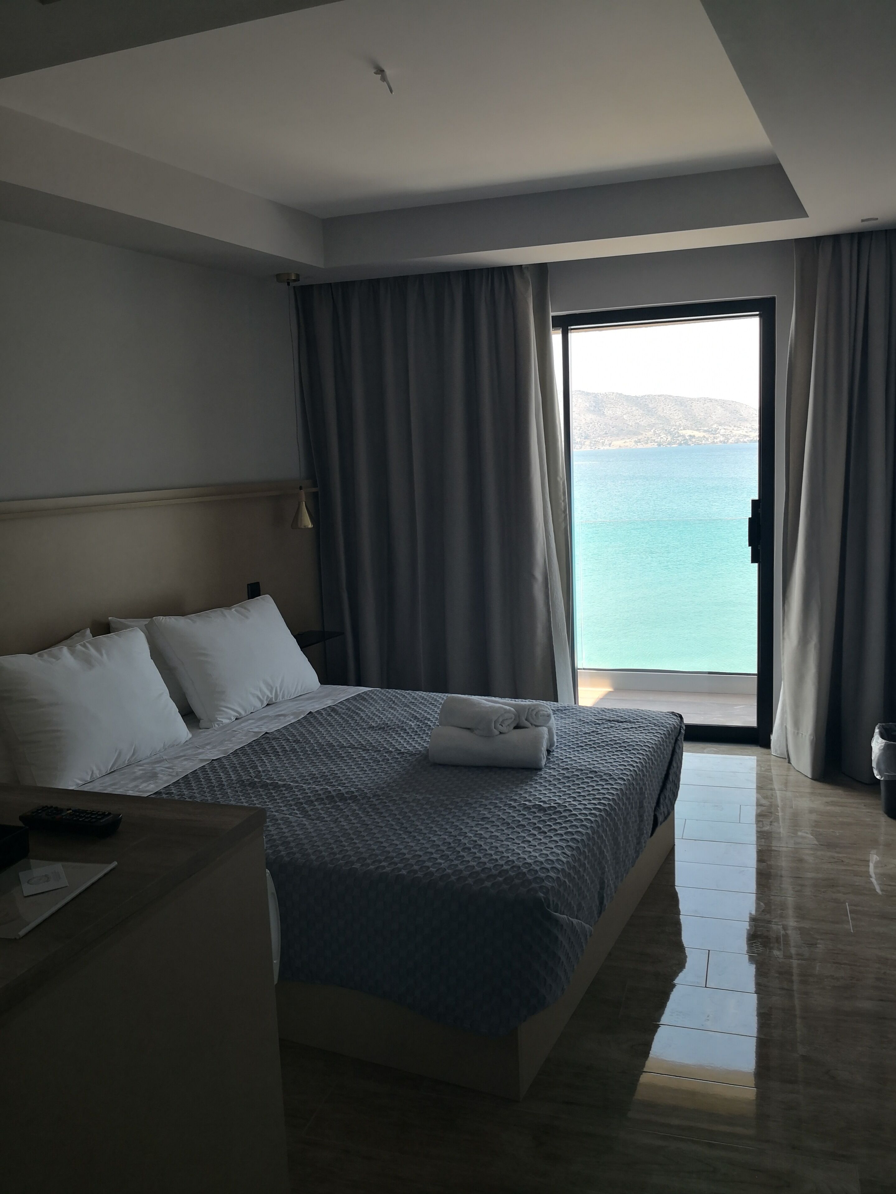 A hotel room with a bed, a desk, and a view of the sea.